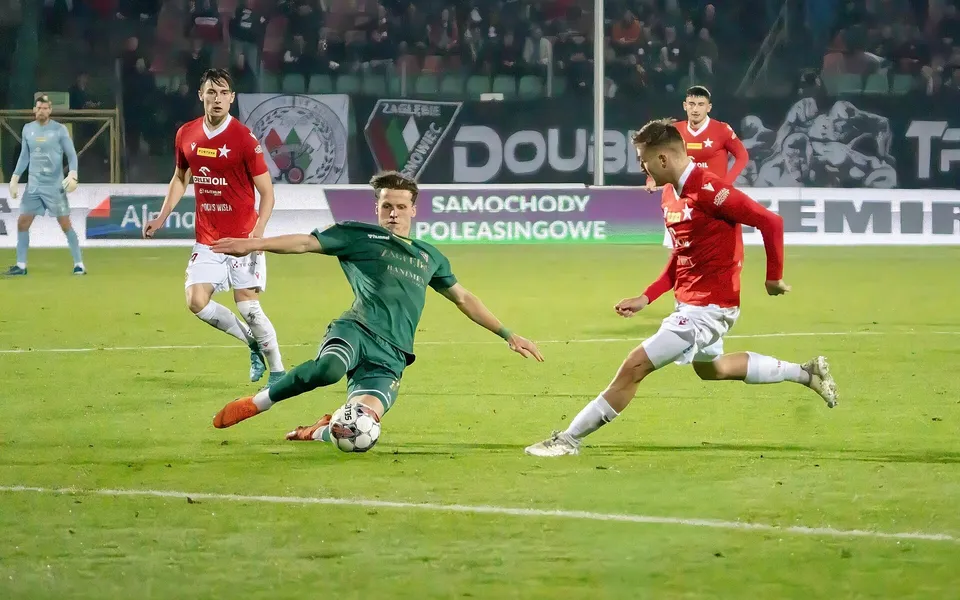 Gece maçında rakip baskısı altında top süren futbolcu