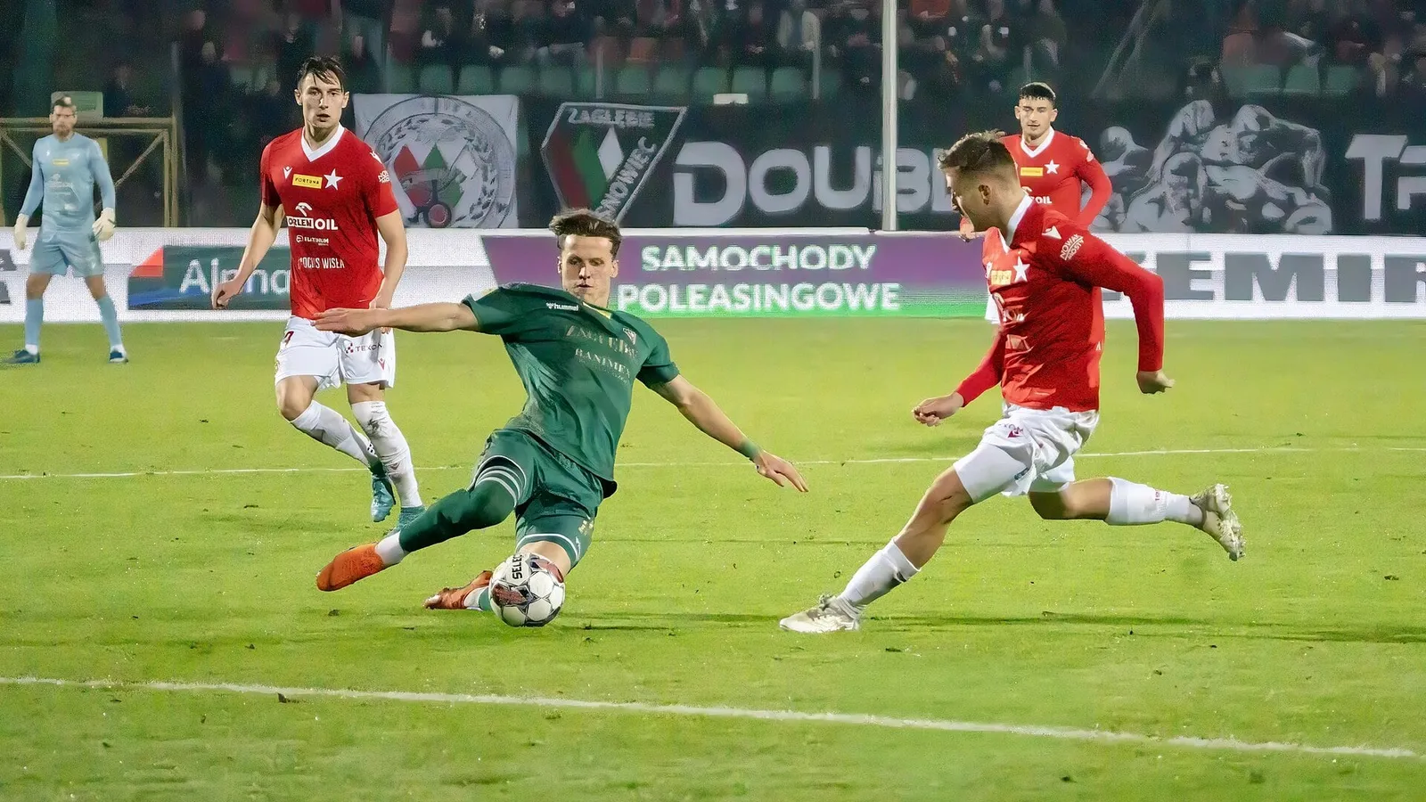 Gece maçında rakip baskısı altında top süren futbolcu